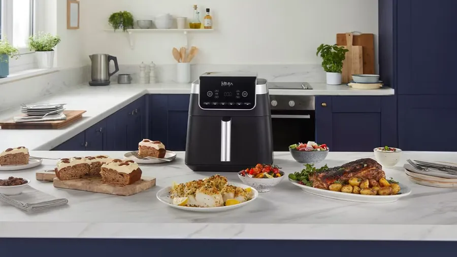 Air fryer posé sur un plan de travail en marbre dans une cuisine bleue, entouré de plats servis pour plusieurs convives