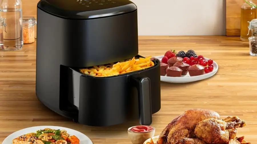 Air fryer noir ouvert avec des frites dorées, accompagné d'un poulet rôti, d'un pavé de saumon aux légumes et de muffins aux fruits rouges