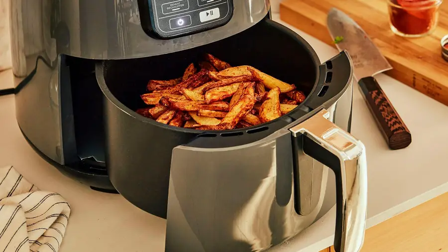 Panier d'air fryer ouvert rempli de quartiers de pommes de terre dorés et épicés, sur un plan de travail de cuisine